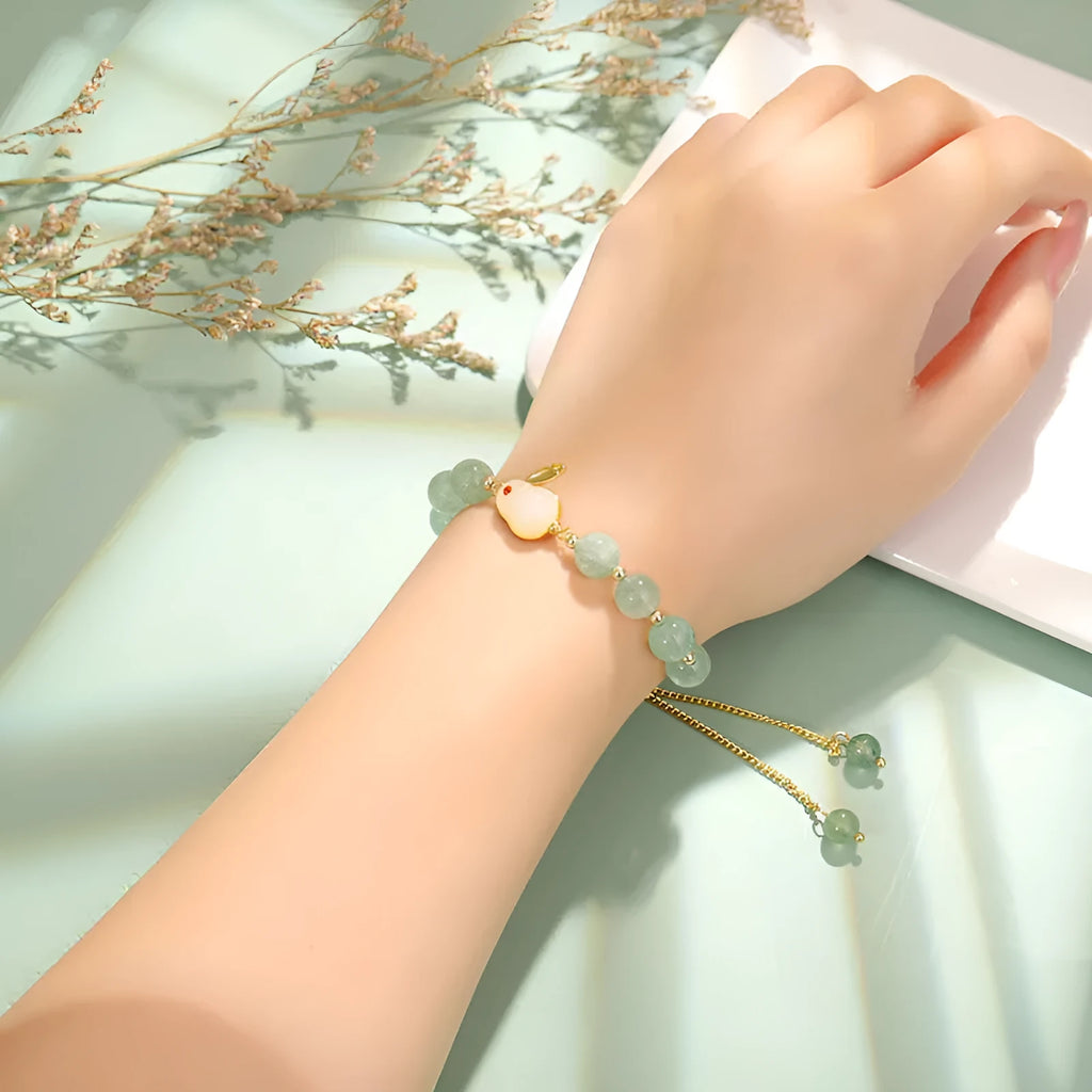 Rabbit charm bracelet with green aventurine or strawberry quartz stones and gold accents on a wrist.