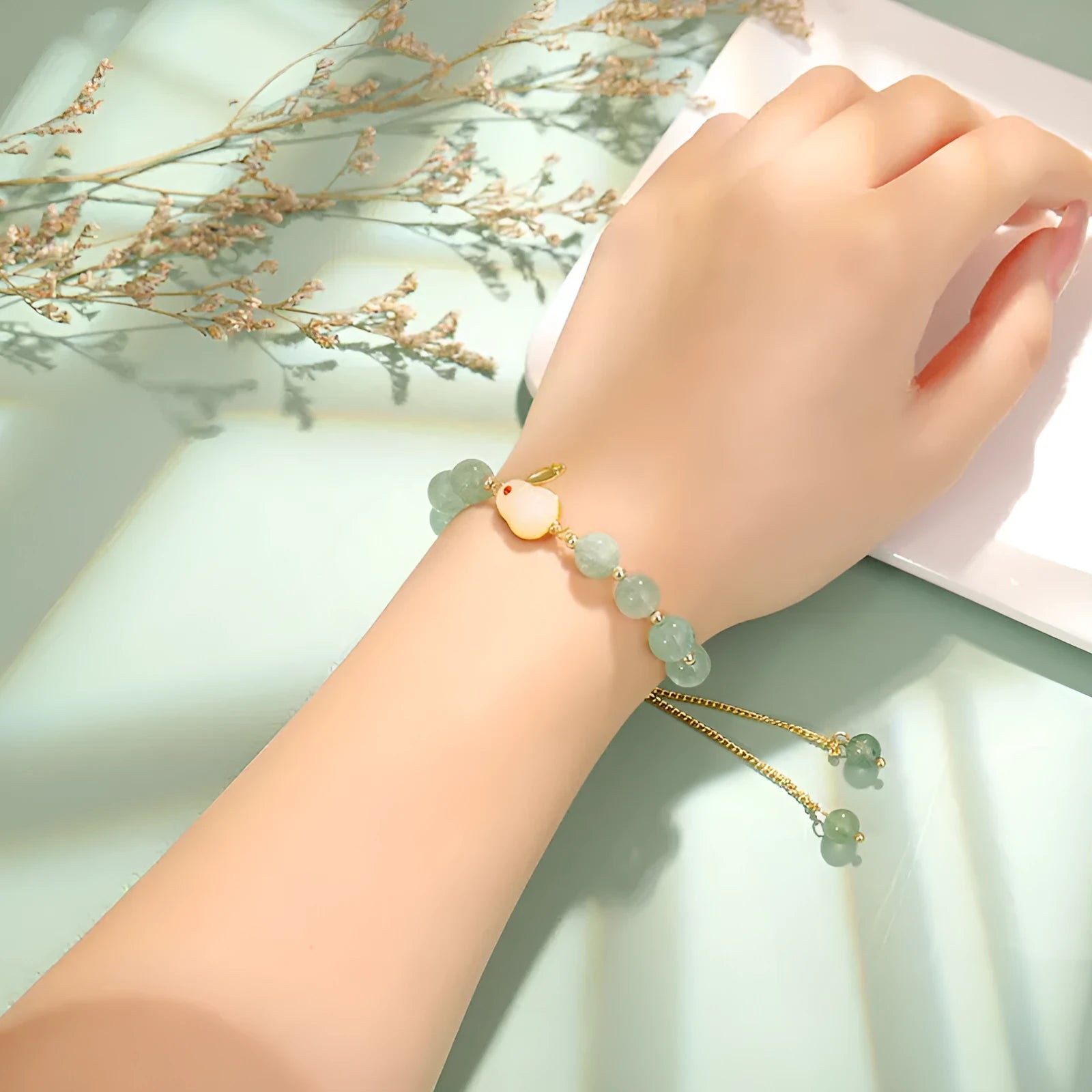 Rabbit charm bracelet with green aventurine or strawberry quartz stones and gold accents on a wrist.