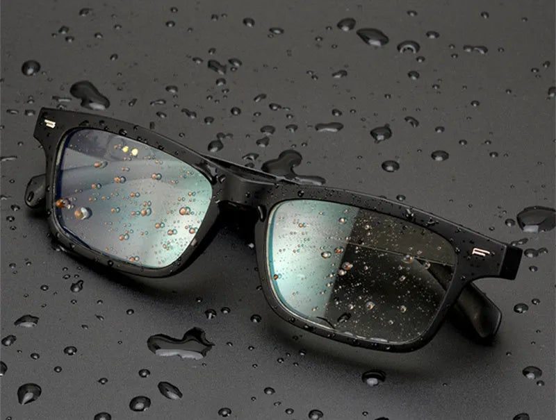 Black Bluetooth smart glasses with semi-open ear speakers and interchangeable lenses on a table with case.