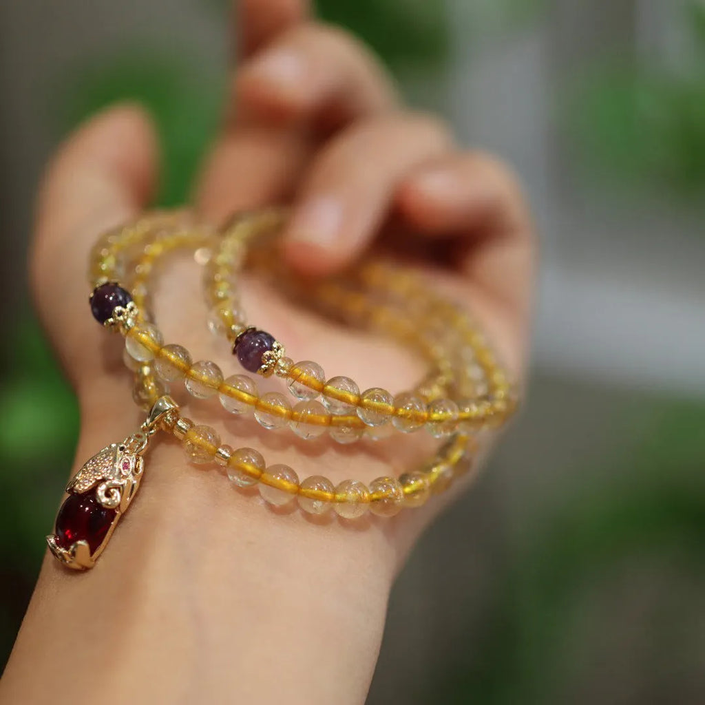 Natural gold rutilated quartz bracelet with three gold circles and a hanging chopstick charm on wrist.