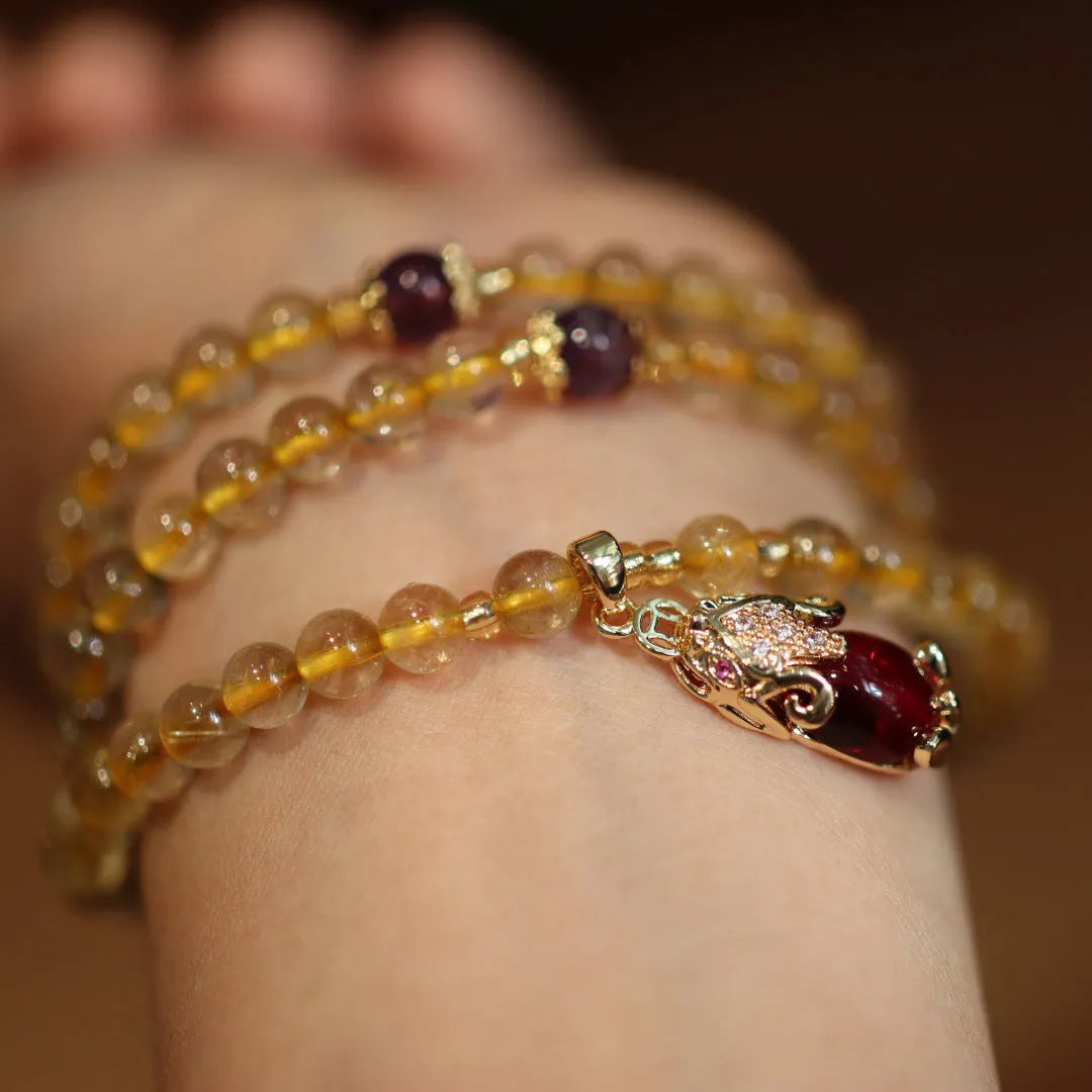 Natural gold rutilated quartz bracelet with three gold circles and a hanging chopstick charm on wrist.