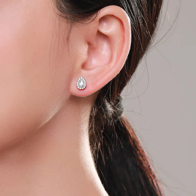 Close-up of a pair of women's silver water drop shaped stud earrings on a plain background.