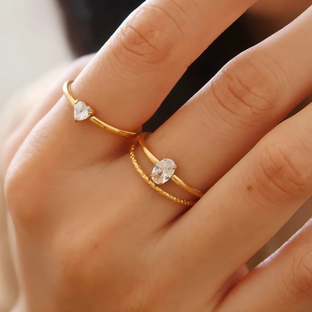 A golden stainless steel ring in a heart shape, shown next to an oval version, on a plain background.