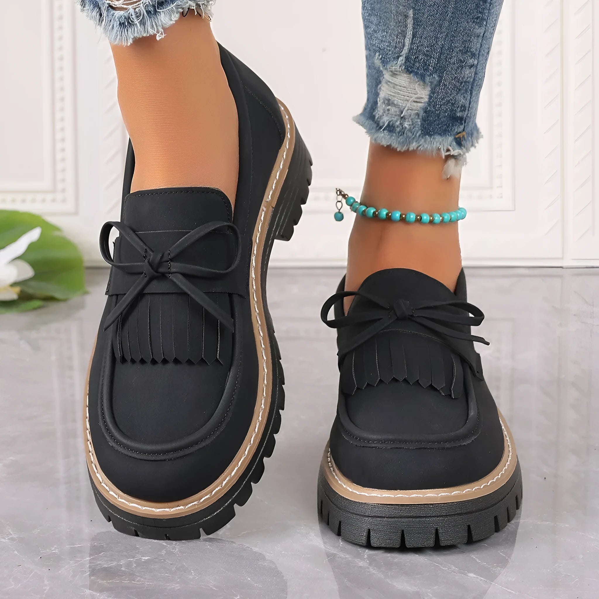 Black and brown women's tassel loafers with a chunky heel and bowknot detail on a rubber sole.