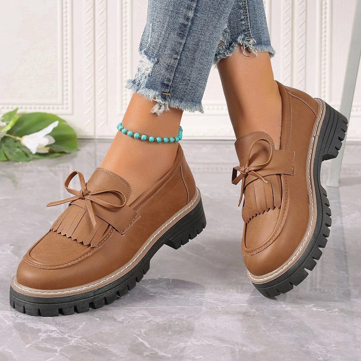 Black and brown women's tassel loafers with a chunky heel and bowknot detail on a rubber sole.