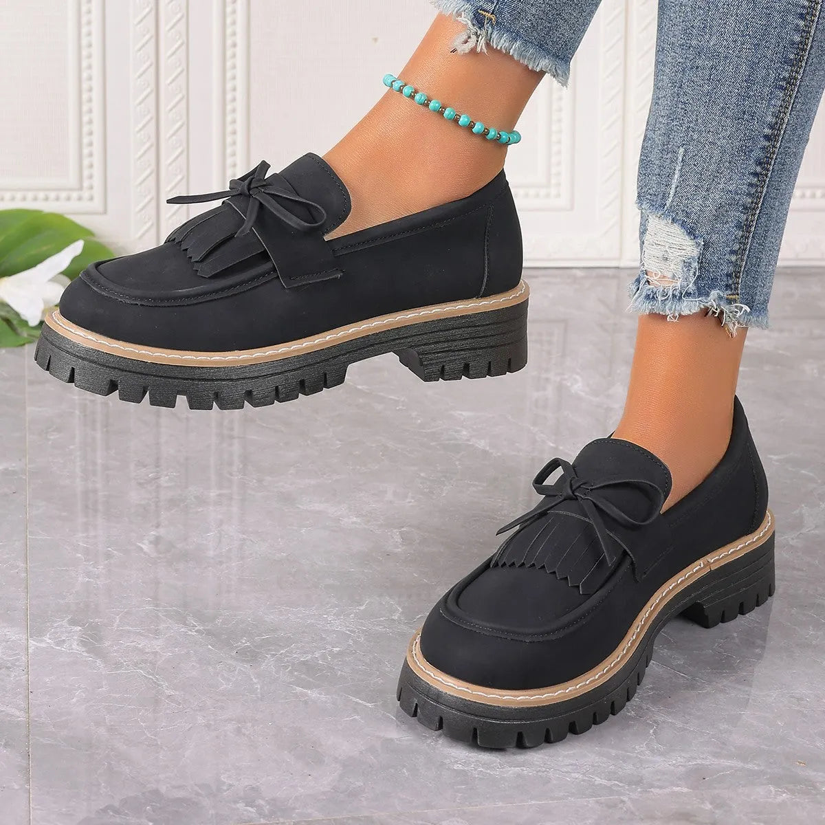 Black and brown women's tassel loafers with a chunky heel and bowknot detail on a rubber sole.