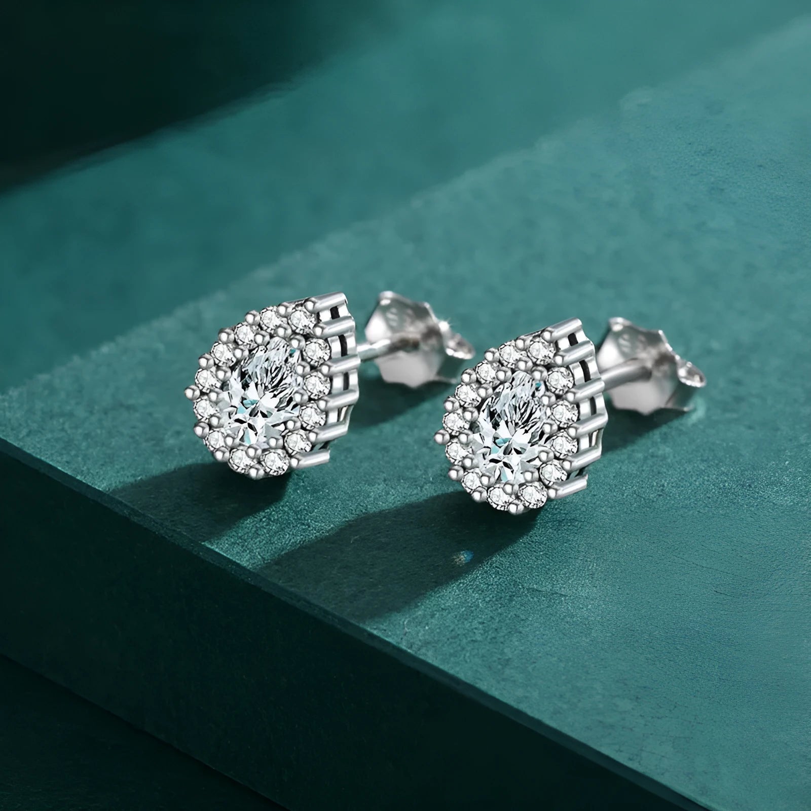 Close-up of a pair of women's silver water drop shaped stud earrings on a plain background.
