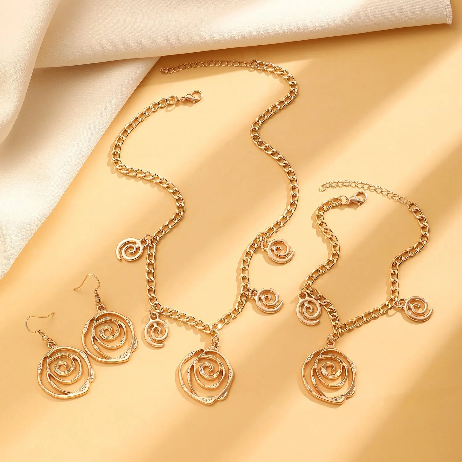 Gold tone donut spiral necklace, bracelet, and earrings set on a white background.