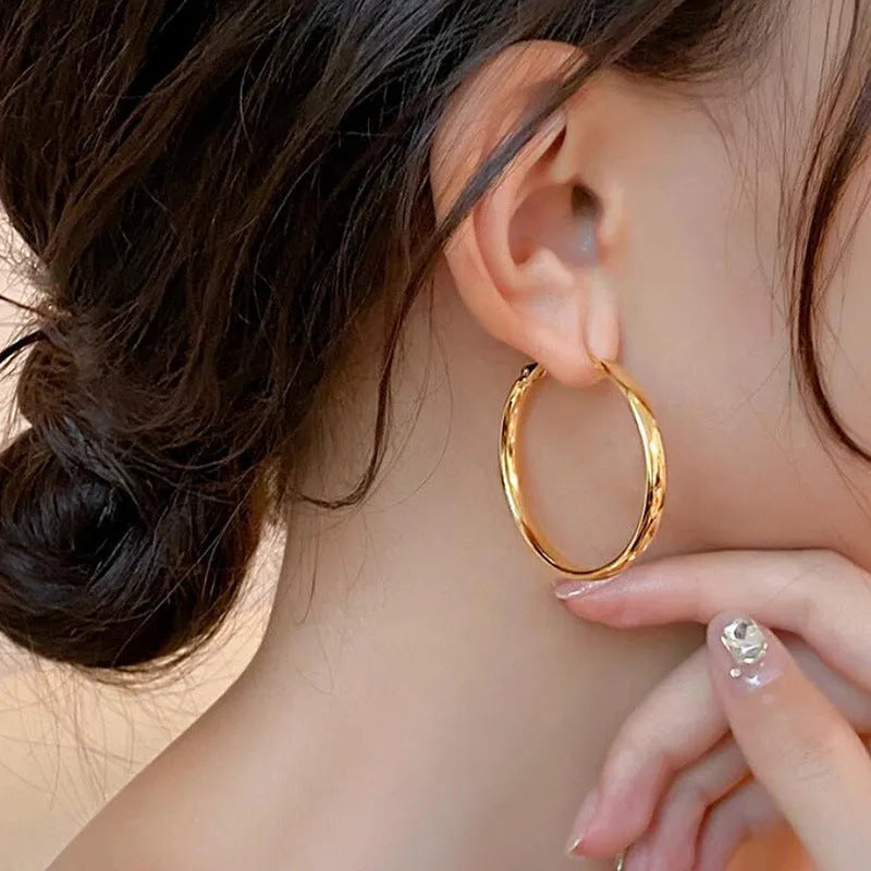 A pair of large gold-coloured metal circle hoop earrings on a white background