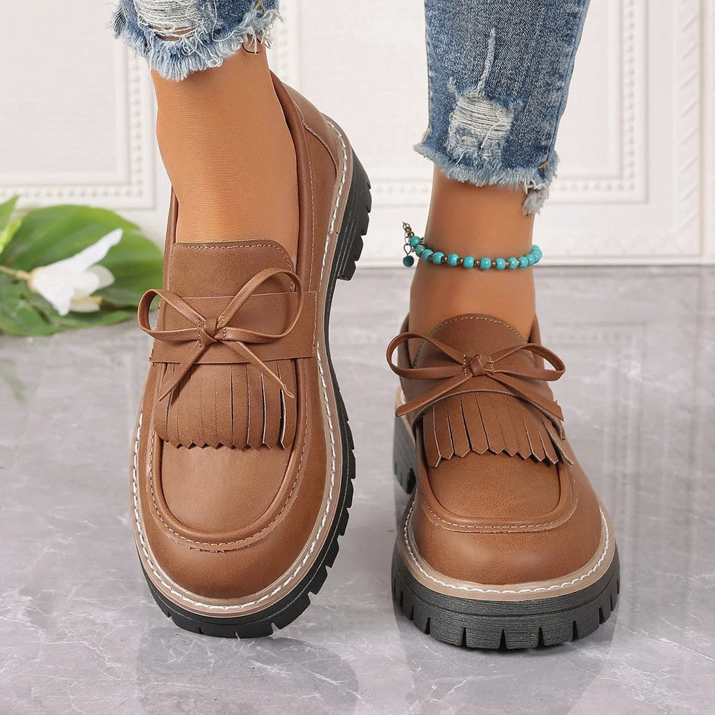 Black and brown women's tassel loafers with a chunky heel and bowknot detail on a rubber sole.
