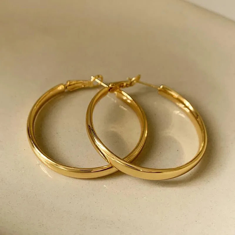 A pair of large gold-coloured metal circle hoop earrings on a white background