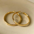 A pair of large gold-coloured metal circle hoop earrings on a white background