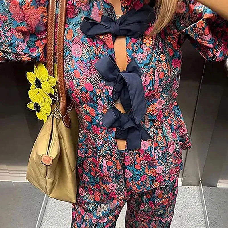Women's floral print two-piece suit with a tie-neck puff sleeve blouse and straight-leg trousers.