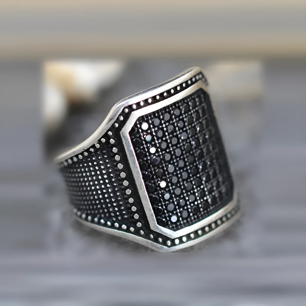 Black alloy ring with copper inlay and zircon stone detailing, shown on a finger.