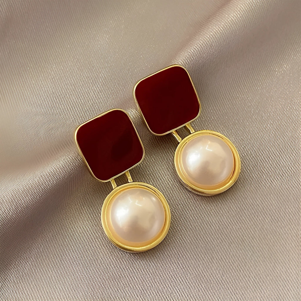 Red geometric alloy stud earrings with pearl centre on white background