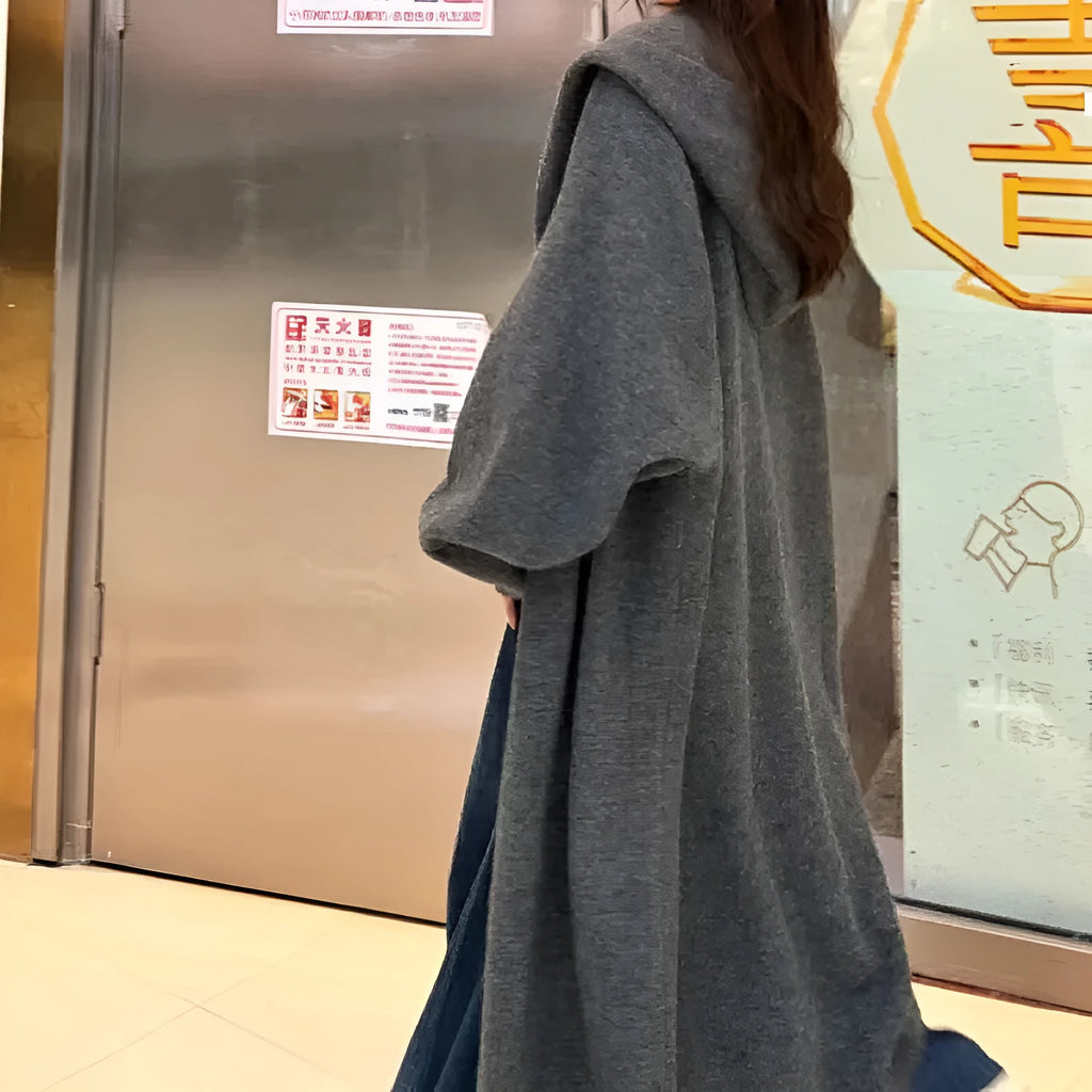 A woman wearing a long, hooded, beige knitted cardigan in a relaxed Korean style.