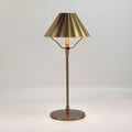 Gold-colour alloy desk lamp with a cylindrical shade on a wooden desk, showing a USB-C charging cable.