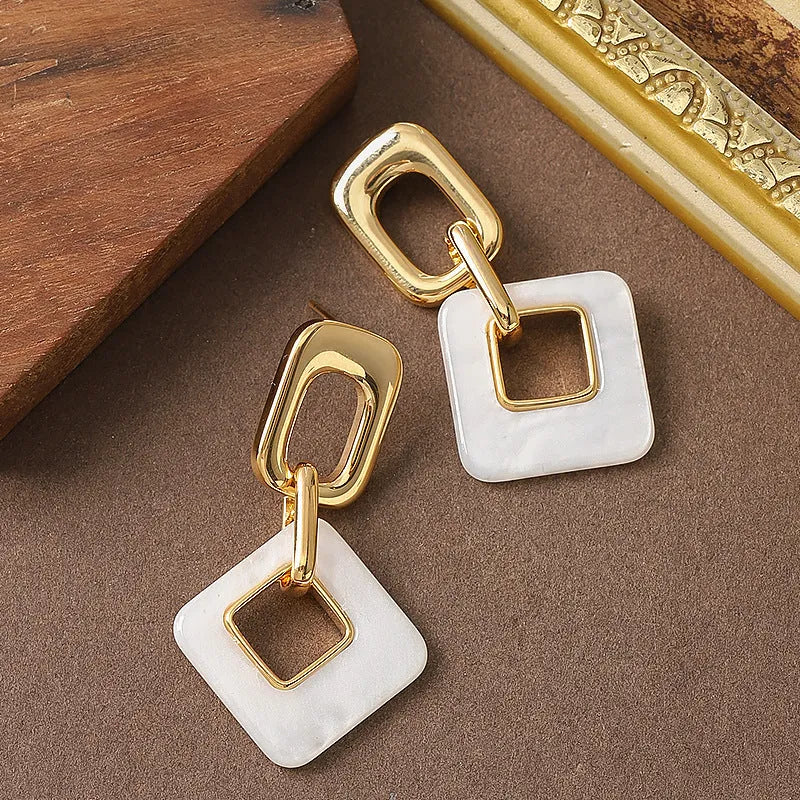 A pair of hollow geometric square earrings with a chamfered pattern, shown in an electroplated finish.