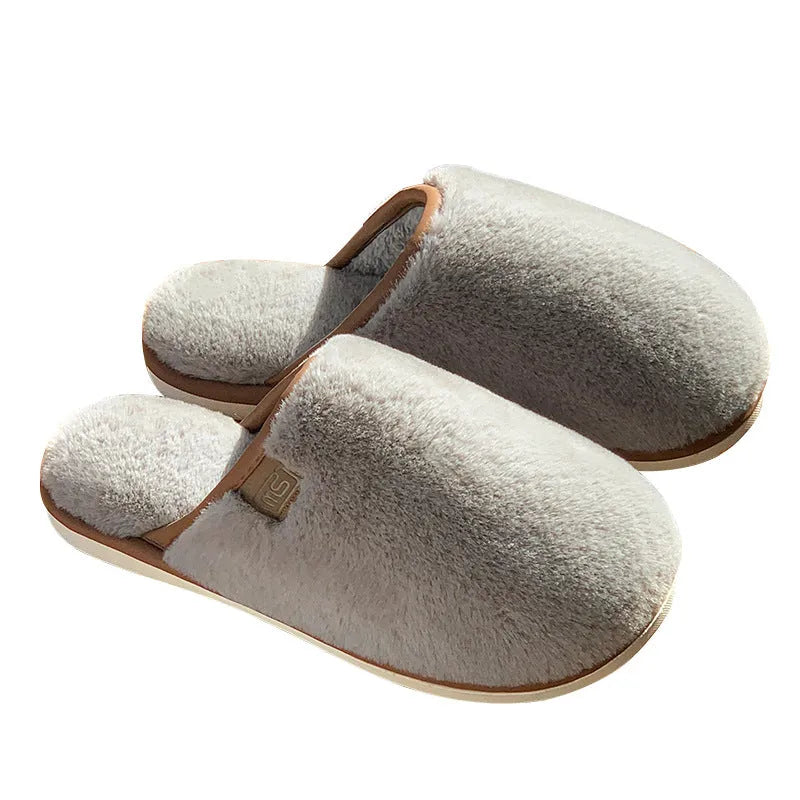 Pair of solid blue plush winter slippers with non-slip PVC sole on a wooden floor.