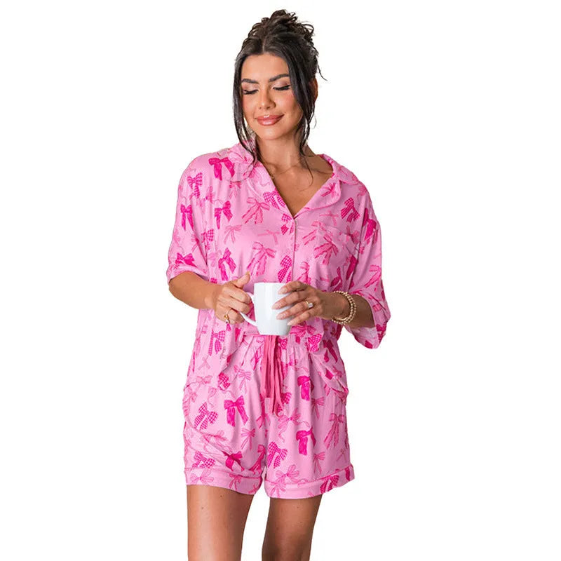 Pink women's pyjama set with bow print, featuring a top and trousers made from lightweight polyester.