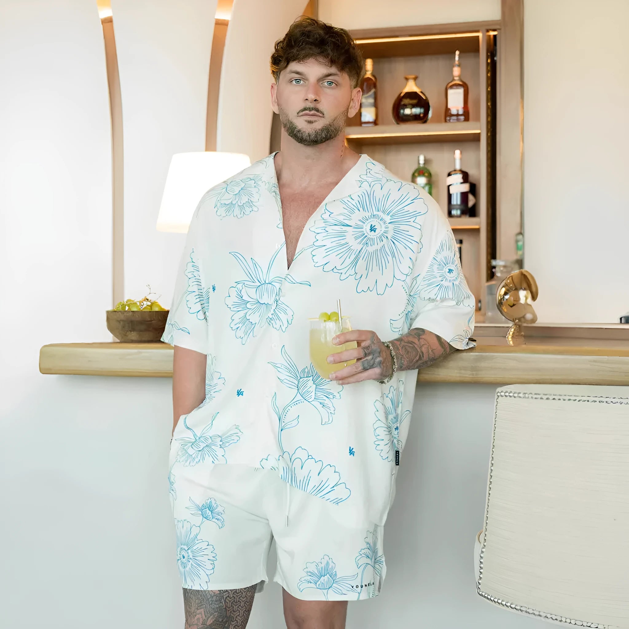 A man's loose-fit short sleeve printed top with a floral pattern, shown in a light colour on a hanger.