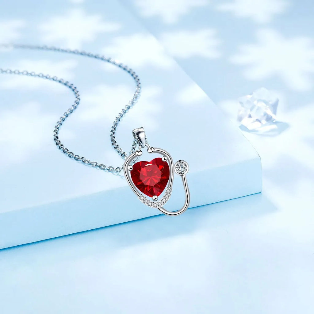 Red diamond women's necklace with a stethoscope, wings, and cross pendant on an adjustable chain.