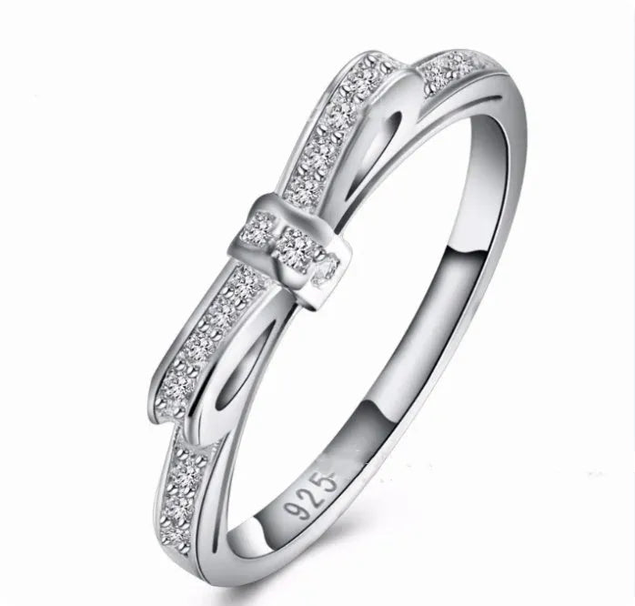 A silver-coloured bow-shaped ring set with sparkling clear rhinestone crystals on a finger.
