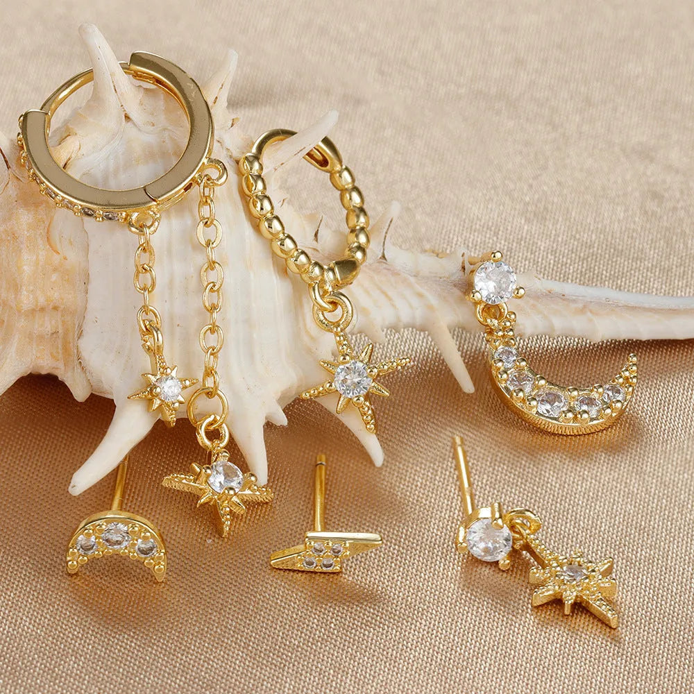 Set of six pairs of gold chain tassel drop earrings with zircon studs laid out on a surface.