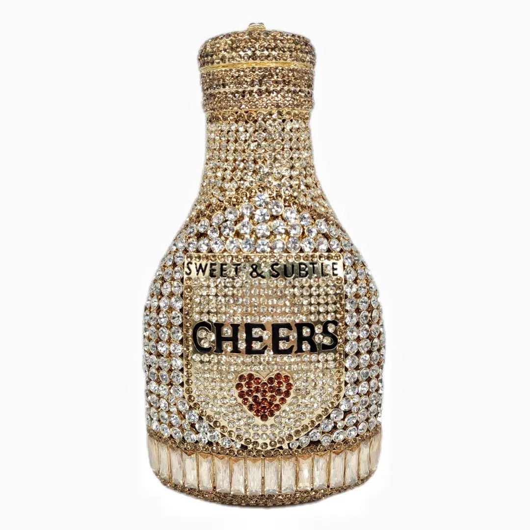 Gold hard-shell clutch bag shaped like a champagne bottle with crystal accents on a black background.