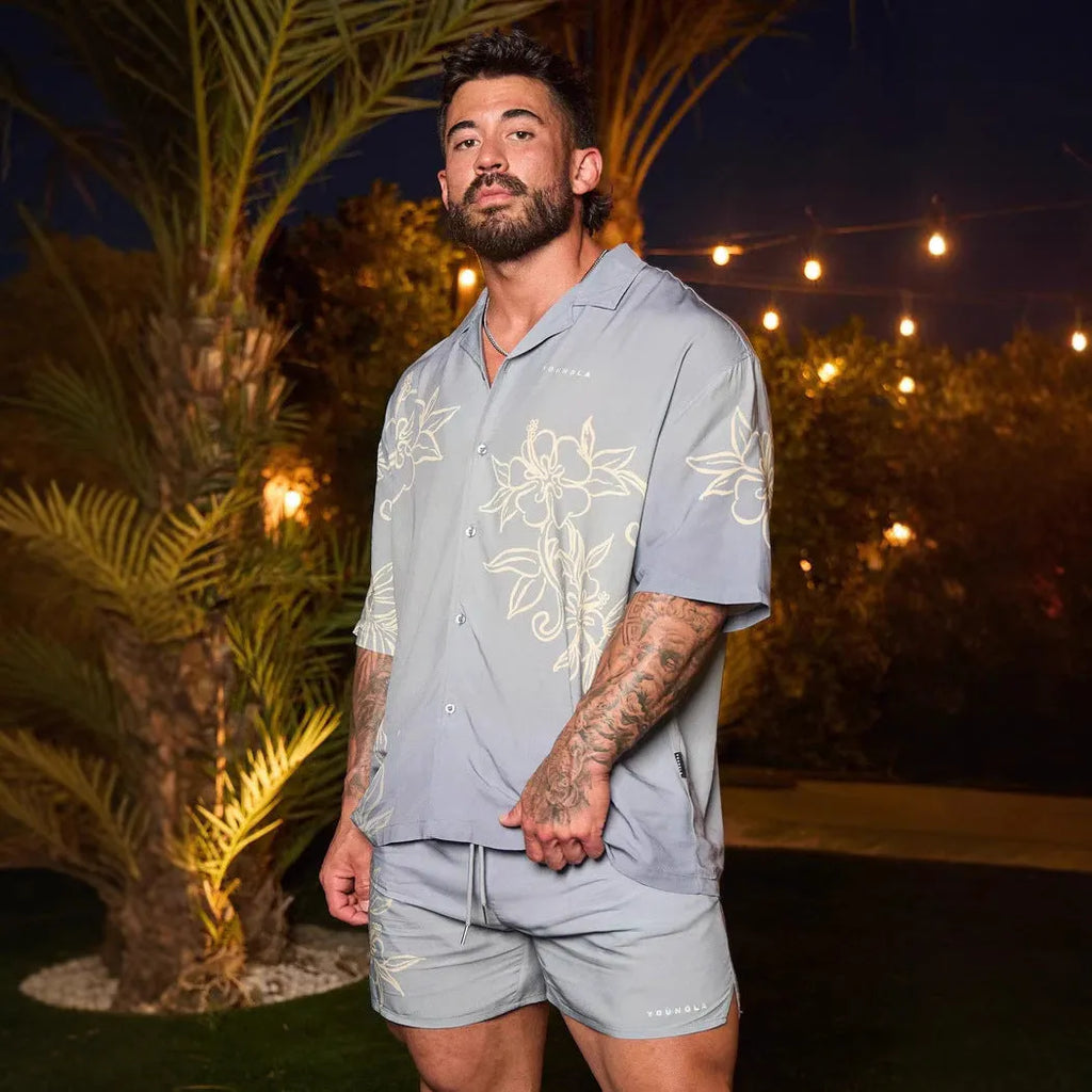 A man's loose-fit short sleeve printed top with a floral pattern, shown in a light colour on a hanger.