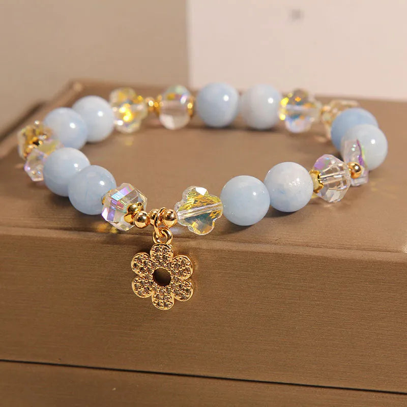 Women's aquamarine crystal bracelet with four-leaf clover charm and pearl details on a wrist.