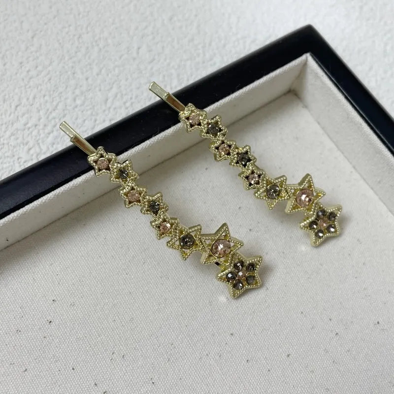 Gold-coloured alloy hair barrette with a side clip, rhinestones, a star, and a word decoration.