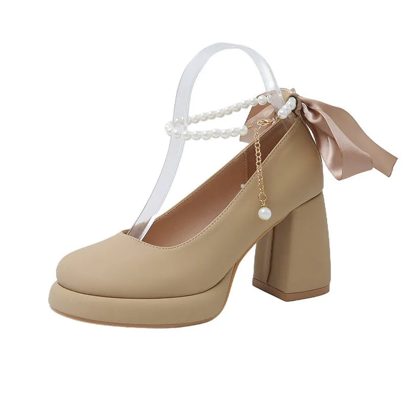 Beige women's Mary Jane shoes with a chunky block heel, ankle strap buckle, and round toe with pearl detail.