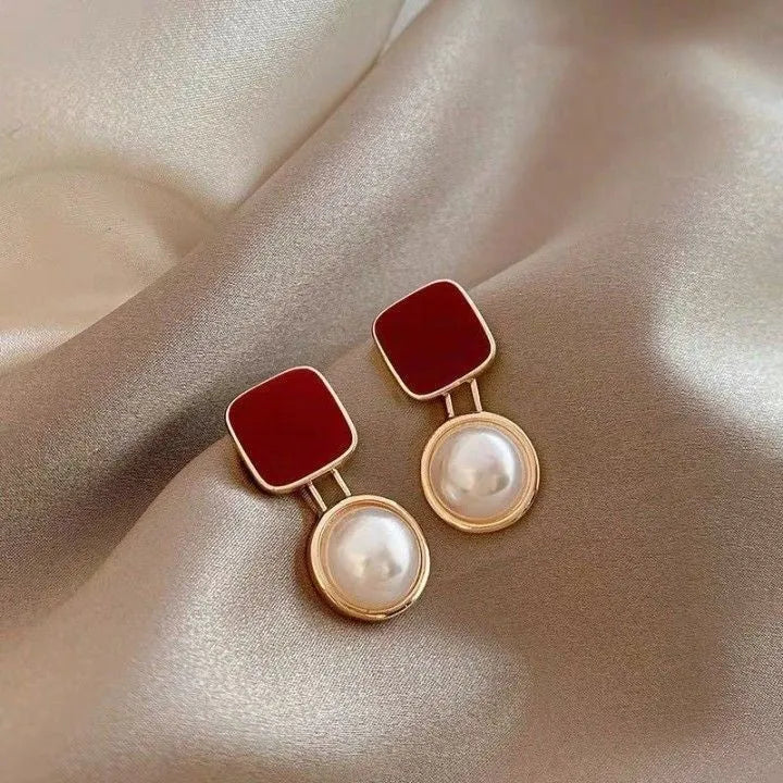 Red geometric alloy stud earrings with pearl centre on white background