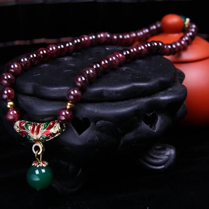 Natural deep red garnet bead bracelet with a golden toad charm, shown in 7mm size on a wrist.