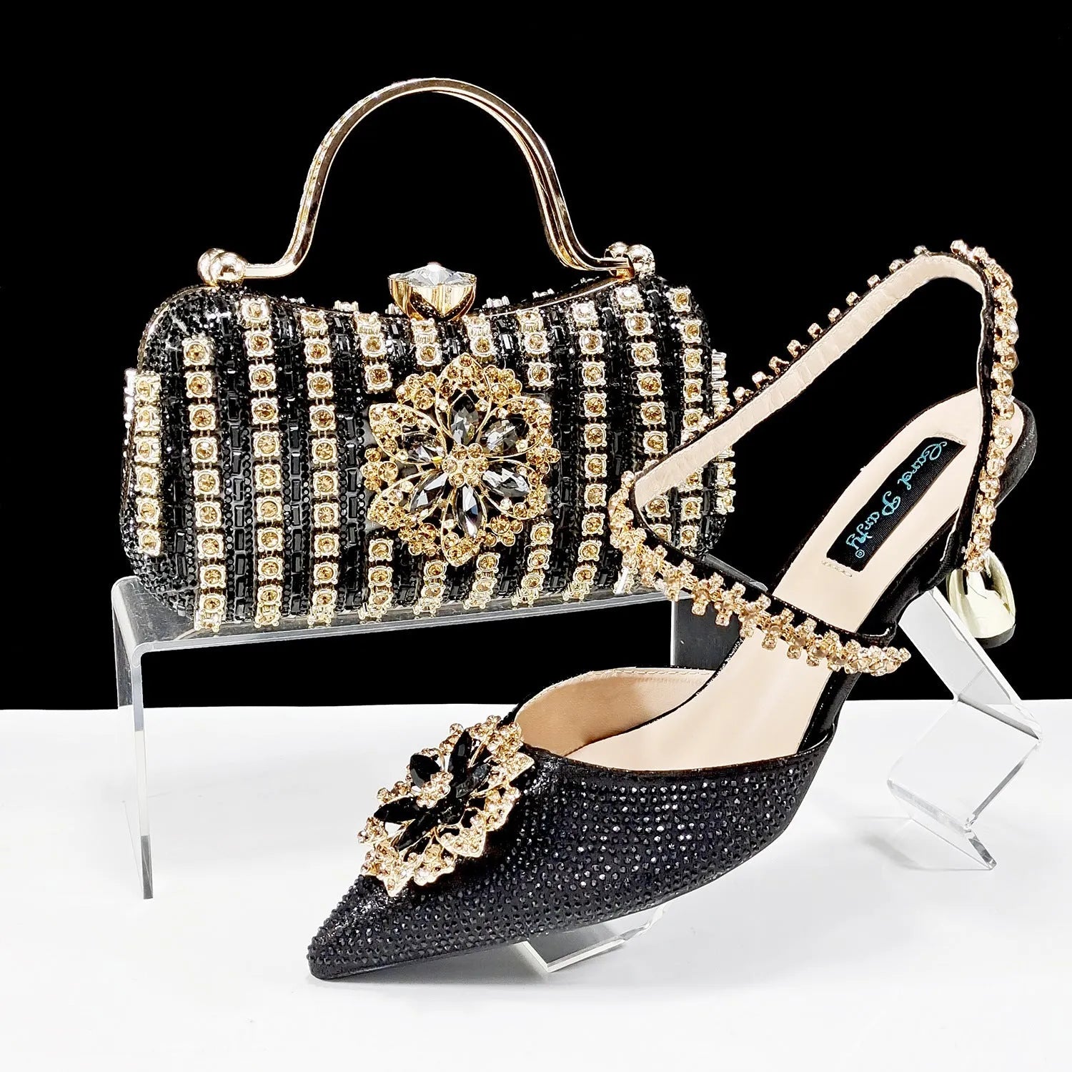 Women's black high heel and matching clutch bag set with rhinestone floral decoration and pointed toe.