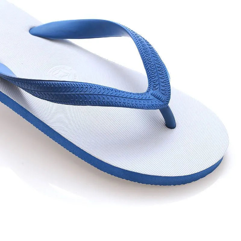 A pair of rubber flip-flops with a fish logo on the strap, shown on a sandy beach.