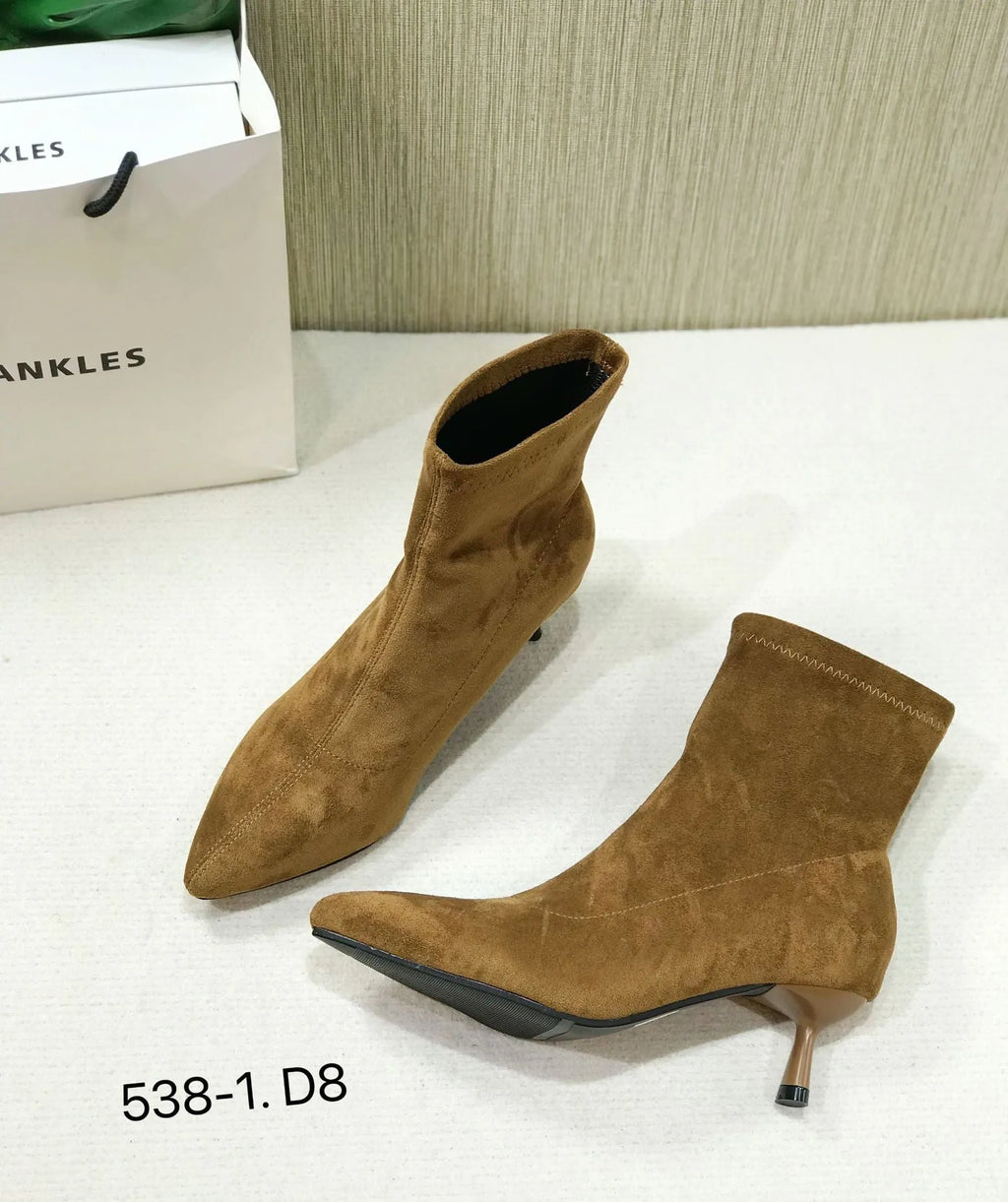 Black pointed toe stiletto ankle boots with a mid-calf sock on a plain background.