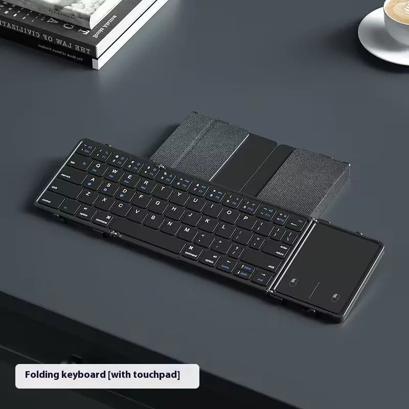 Black folding Bluetooth keyboard shown in open position next to mobile phone