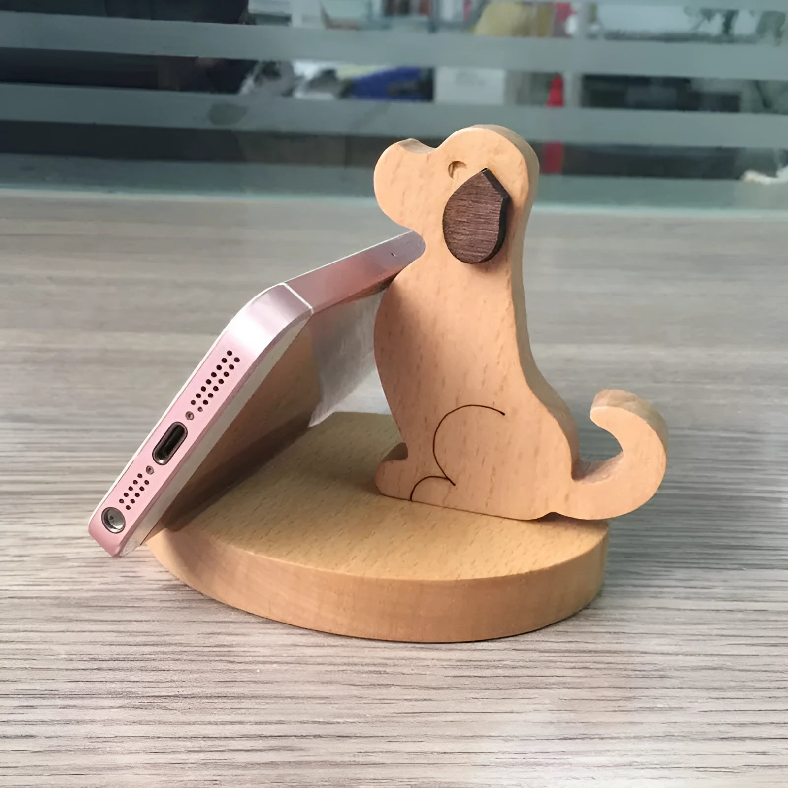 Solid wood cartoon puppy phone bracket with brown spray paint on a desk holding a smartphone upright.