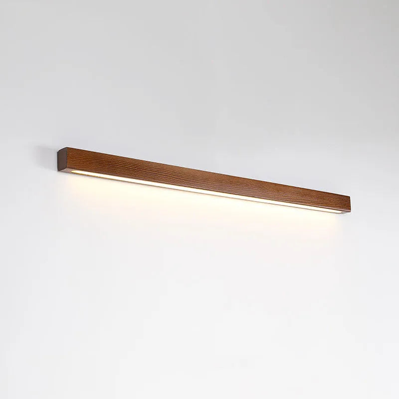 Walnut-coloured linear wood and acrylic strip wall lamp mounted on a light wall.