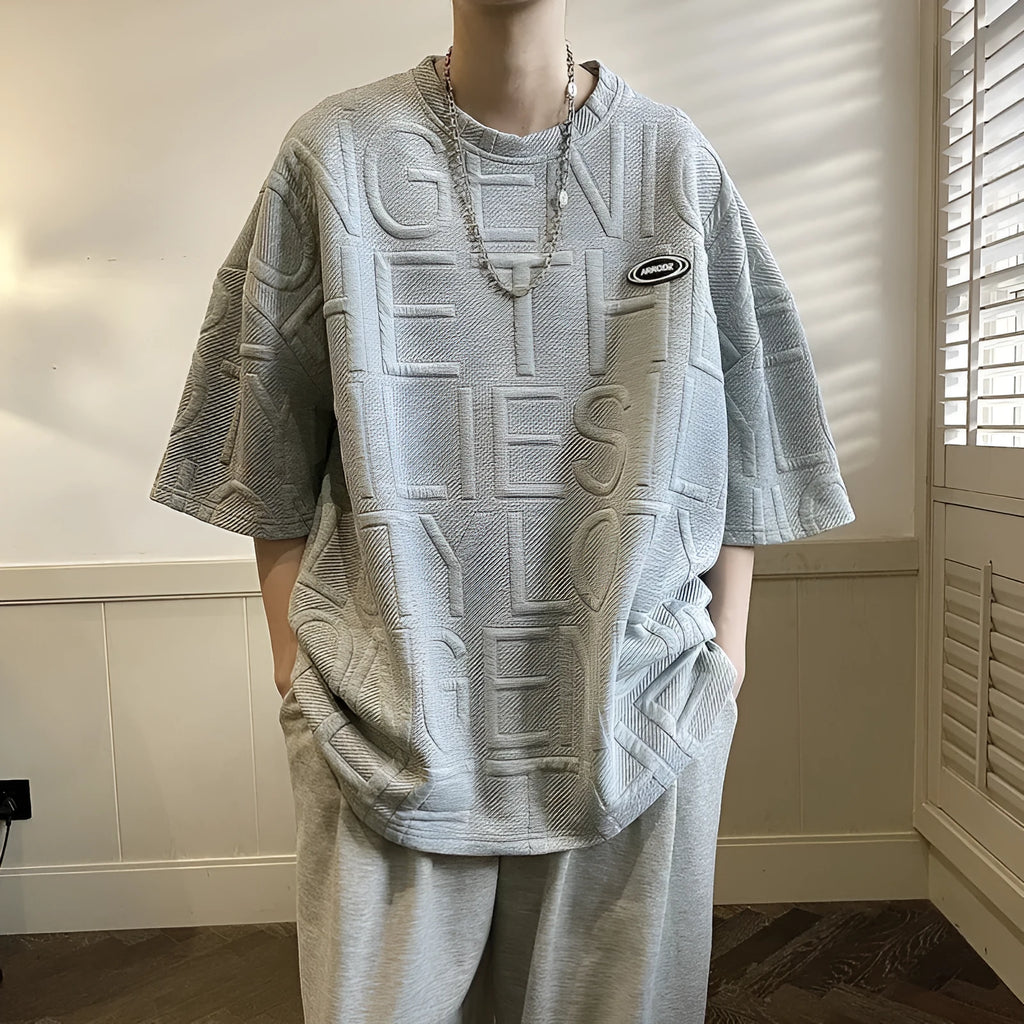 Men's grey loose-fit t-shirt with a raised black three-dimensional letter print on the front.
