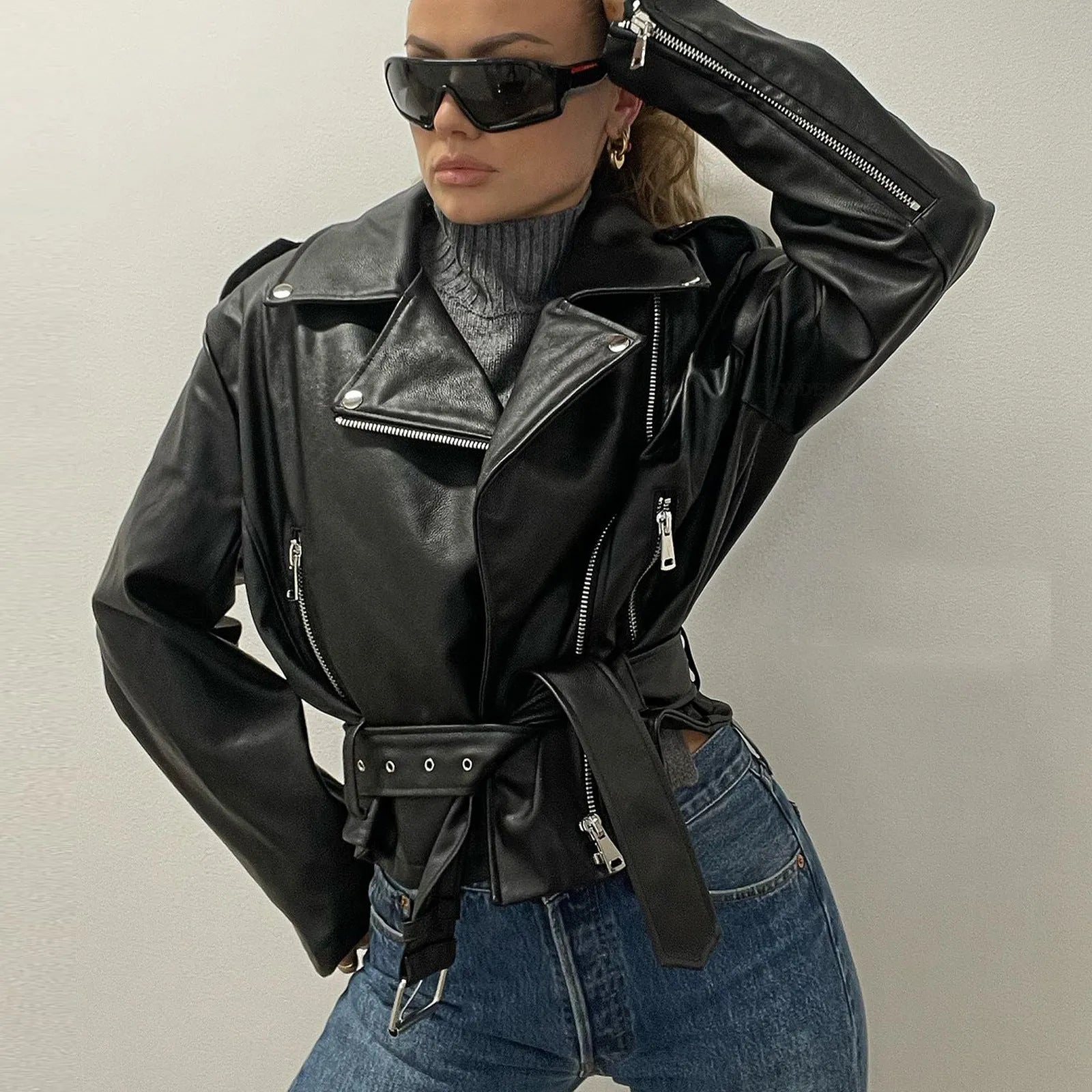 Black punk style jacket with a short belt, lapel, and Peter Pan collar on a hanger.