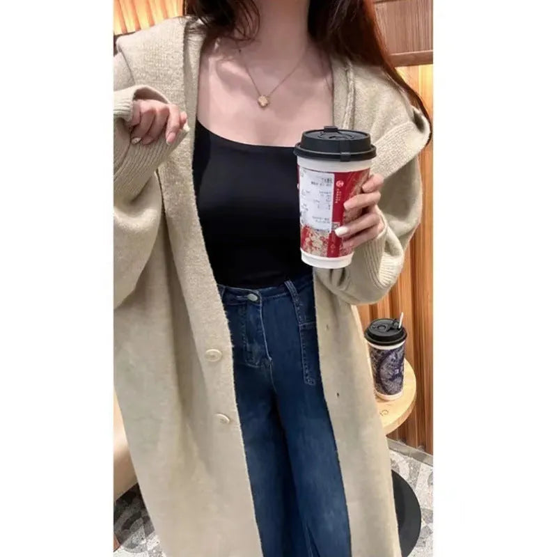 A woman wearing a long, hooded, beige knitted cardigan in a relaxed Korean style.
