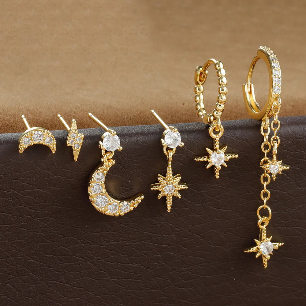 Set of six pairs of gold chain tassel drop earrings with zircon studs laid out on a surface.
