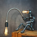 American industrial style table lamp with water pipe design and black iron shade on a wooden desk.