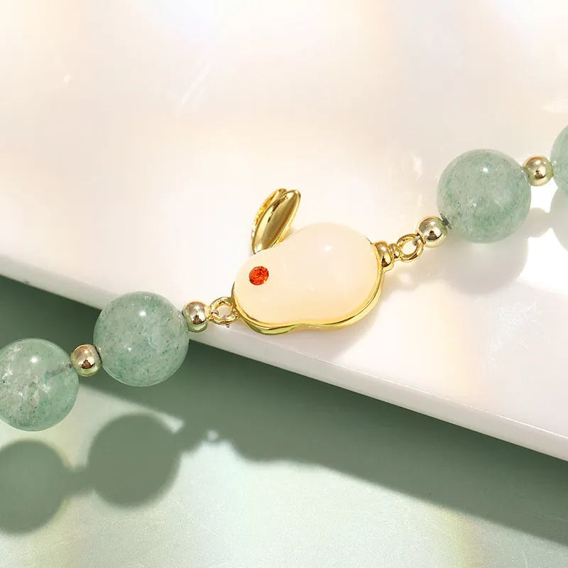 Rabbit charm bracelet with green aventurine or strawberry quartz stones and gold accents on a wrist.