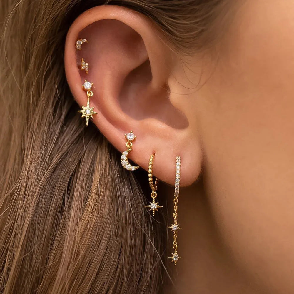 Set of six pairs of gold chain tassel drop earrings with zircon studs laid out on a surface.