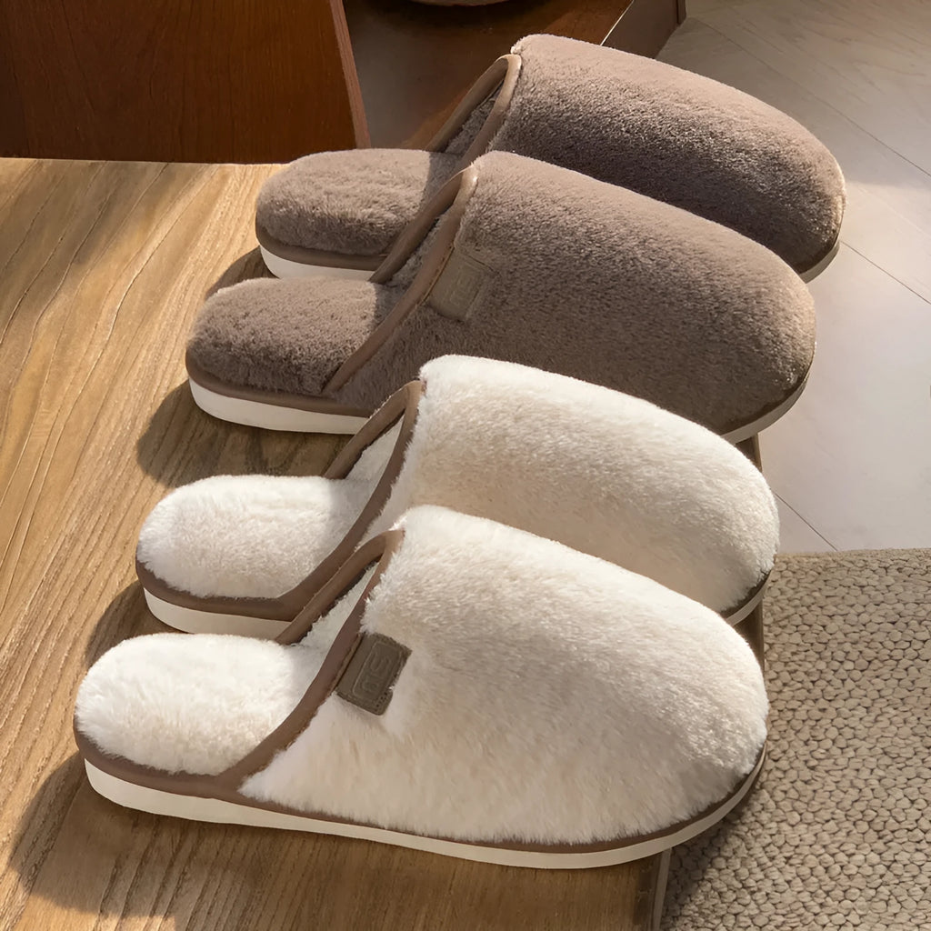 Pair of solid blue plush winter slippers with non-slip PVC sole on a wooden floor.