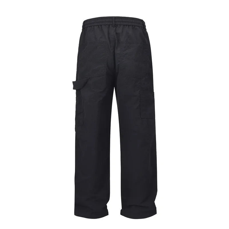 Men's black baggy paratrooper pants with a drawstring waist on a neutral background.